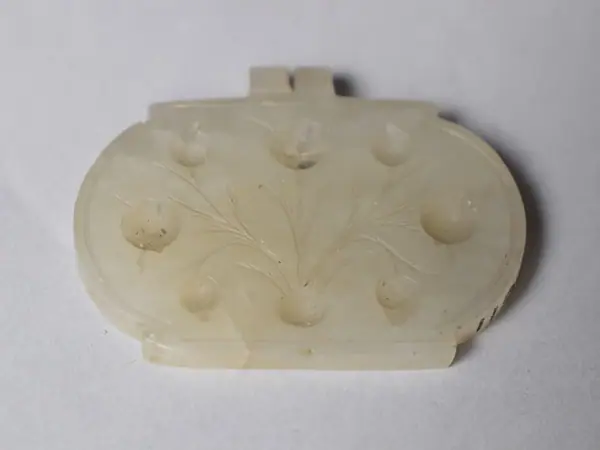 Amulet, generally oval, white nephrite jade, engraved with floral design and cavities for inset stones, India