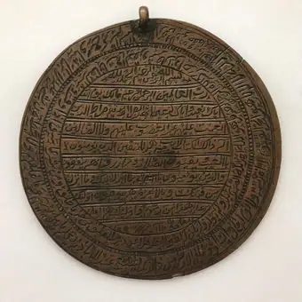 A brass circular amulet with engraved Arabic prayers, possibly Iran